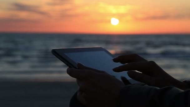 Крупним планом жінка рука використовує планшет на морі на сонячному світлі і фоні під час заходу сонця і океану — стокове відео