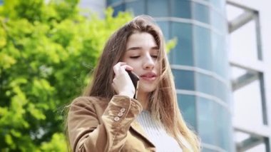 Uzun saçlı, gülümseyen, cep telefonuyla konuşan çekici bir kız. Şehir caddesinde dikilirken. Cep Telefonu Konuşan Güzel Kadın, Şehir Konsepti