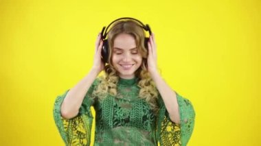 Güzel, mutlu, kulaklıklı, müzik dinleyen ve sarı arka planda dans eden genç bir kadın.