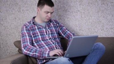 Genç Adam, bir koltukta otururken dizüstü bilgisayarla çalışıyor. İnternette geziniyor, sosyal medyayı kullanıyor ve gevşetiyor..
