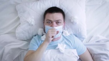 Tıbbi maskeli bir adam yatakta grip yüzünden öksürüyor. Boğazı ağrıyan tıbbi maskeli hasta bir adam. Coronavirus Covid-19. Sağlık kavramı