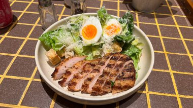 Izgara tavuk ve salatalı bir tabak yemek. Tabak sarı arka planı olan bir masanın üzerinde.