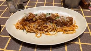 Et soslu ve peynirli bir tabak spagetti bolonez. Tabak masanın üstünde. Tabak beyaz, sos kırmızı.