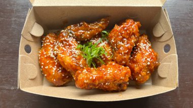 Üzerinde susam tohumları olan bir kutu Yangnyeom tavuk kanadı..