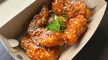 Üzerinde susam tohumları olan bir kutu Yangnyeom tavuk kanadı..