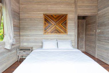 Tahta bir yatak başlığı ve tahta bir duvarı olan beyaz bir yatak. Yatak yapılmamış ve oda boş.