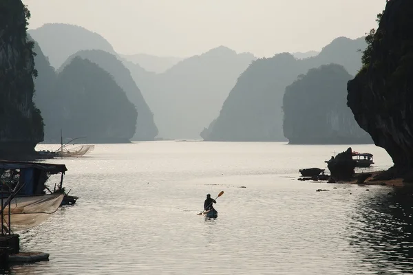 Un hombre remando un pequeño bote en el mar con montañas en el fondo —  Fotos de Stock