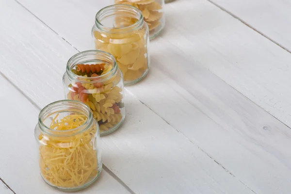 Various pasta in jars on the white  wooden table. — Stock Photo, Image
