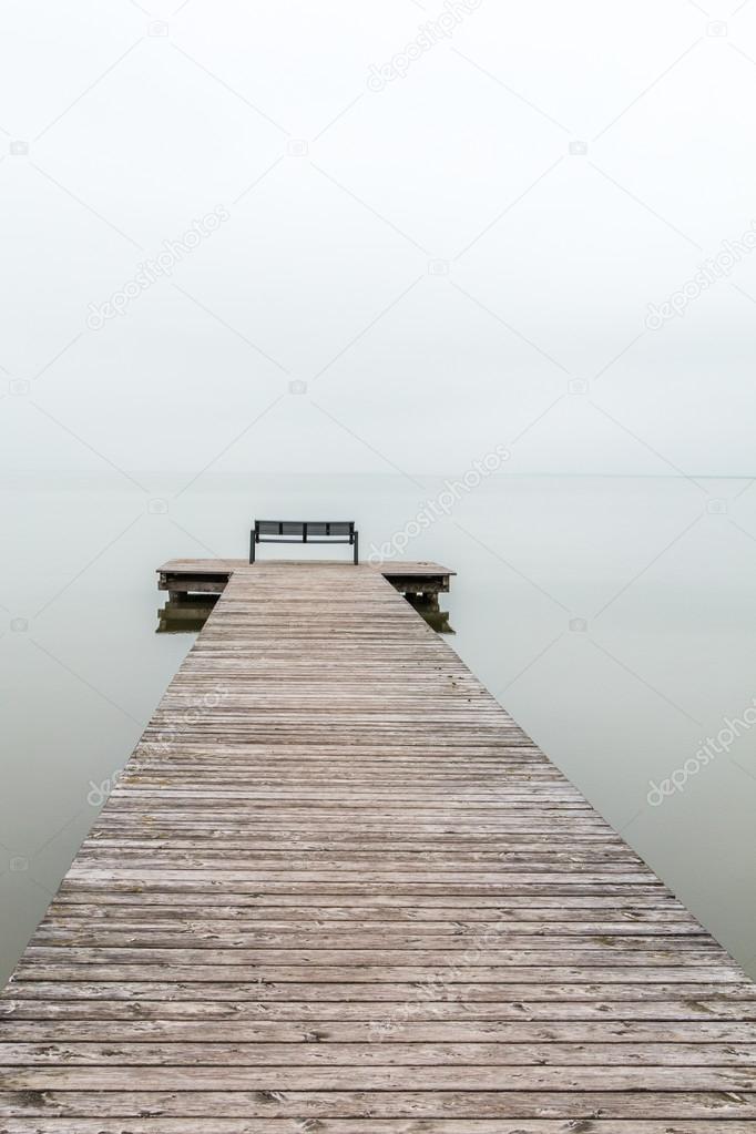 Jetty in foggy weather with bench at end