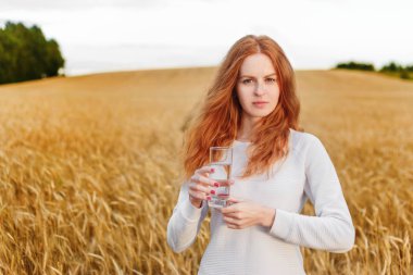 Alanını ayakta ve içme suyu ile bir bardak tutan genç Kızıl saçlı kadın.