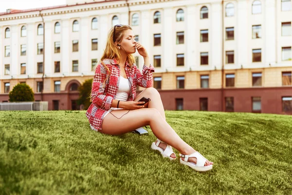 잔디에 앉아있는 동안 헤드폰을 착용 하는 닫힌된 눈으로 음악을 즐기는 금발. — 스톡 사진