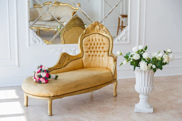 Poltrona vintage elegante em um quarto espaçoso com ornamentos decorados na parede e espelho. flores coloridas em vaso de pé no chão de madeira — Fotografia de Stock