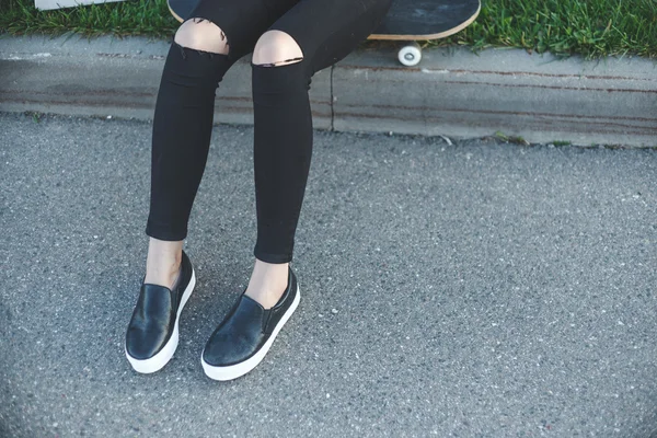 Kvinnans ben i jeans, sneakers bredvid henne skateboard utomhus — Stockfoto