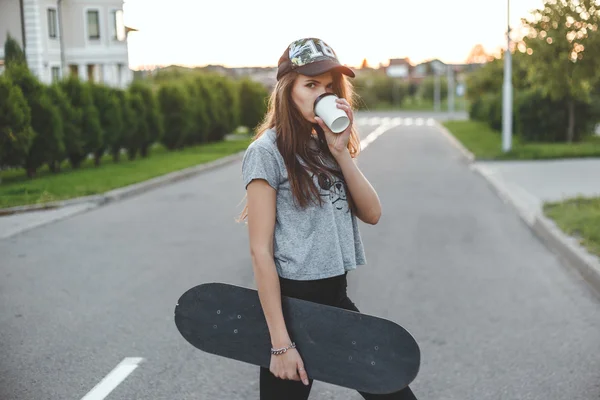 A menina com um estilo de vida ativo começa de manhã com café e skate . — Fotografia de Stock