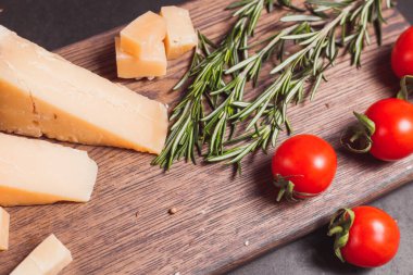 Parmesan peyniri, taze domates ve tahta üzerinde bitkiler.