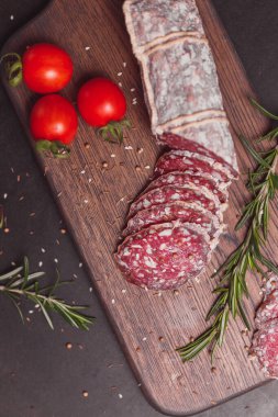 Koyu ahşap tahtada füme jambon ve biberiye ve kiraz domatesli dilimler. Üst görünüm, düz görünüm