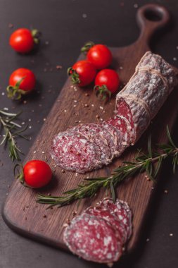 Koyu ahşap tahtada füme jambon ve biberiye ve kiraz domatesli dilimler. Üst görünüm, düz görünüm