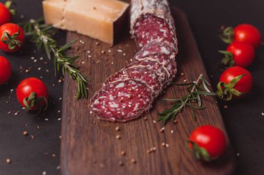 Koyu ahşap tahtada füme jambon ve biberiye ve kiraz domatesli dilimler.