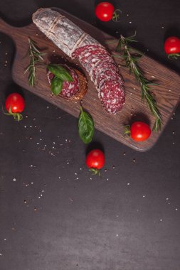 Koyu ahşap tahtada füme jambon ve biberiye ve kiraz domatesli dilimler. Üst görünüm, düz görünüm