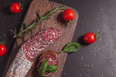 Koyu ahşap tahtada füme jambon ve biberiye ve kiraz domatesli dilimler.