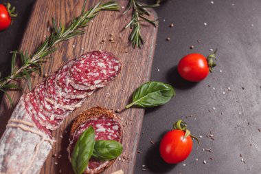 Koyu ahşap tahtada füme jambon ve biberiye ve kiraz domatesli dilimler. Üst görünüm, düz görünüm