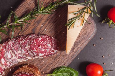 Koyu ahşap tahtada füme jambon ve biberiye ve kiraz domatesli dilimler. Üst görünüm, düz görünüm