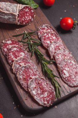 Koyu ahşap tahtada füme jambon ve biberiye ve kiraz domatesli dilimler.