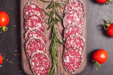 Koyu ahşap tahtada füme jambon ve biberiye ve kiraz domatesli dilimler. Üst görünüm, düz görünüm