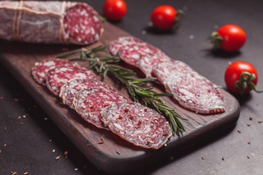 Koyu ahşap tahtada füme jambon ve biberiye ve kiraz domatesli dilimler.