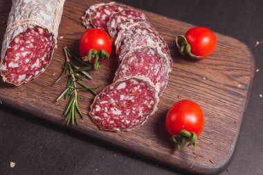 Koyu ahşap tahtada füme jambon ve biberiye ve kiraz domatesli dilimler.