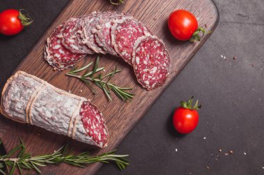 Koyu ahşap tahtada füme jambon ve biberiye ve kiraz domatesli dilimler. Üst görünüm, düz görünüm