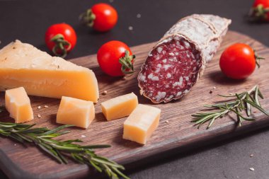 Koyu ahşap tahtada füme jambon ve biberiye ve kiraz domatesli dilimler.