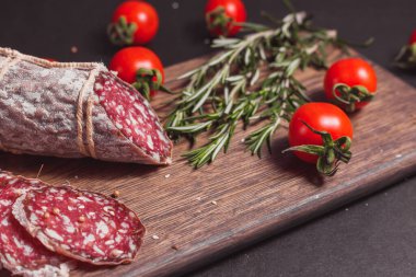 Koyu ahşap tahtada füme jambon ve biberiye ve kiraz domatesli dilimler.