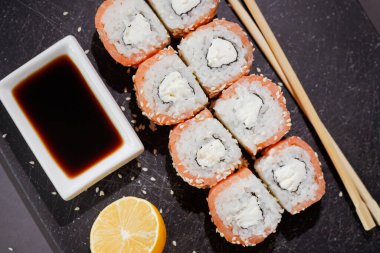 Suşi ruloları, koyu arkaplanda limon ve az pişmiş olarak servis edilir. Siyah üzerine düz düzen, üst görünüm