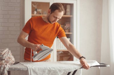 Evdeki ütü masasında çocuk çarşaflarını ütüleyen genç adam.
