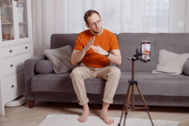 Hipster blogger cep telefonuyla video kaydediyor. oturma odasındaki koltuğa otur ve el kol hareketi yap.