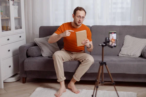 Hombre guapo blogger en casa presenta libro mientras flujo de vídeo. Marketing en redes sociales y ventas en línea — Foto de Stock