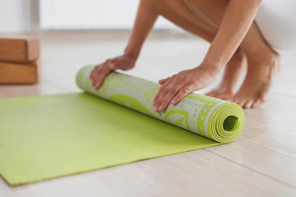 Una mujer descalza tuerce la esterilla de yoga verde y la aptitud en el suelo de parquet. —  Fotos de Stock