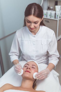 Doktor güzellik uzmanı güzellik salonunda yüz derisini süngerle temizliyor..