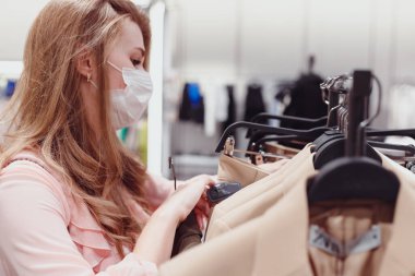 Giyim mağazasından koruyucu yüz maskesi takan güzel bir bayan müşteri. Moda Mağazasındaki Çeşitli İnsanlar, Şık Kıyafetler Seçimi, Renkli Sürdürülebilir Markalar