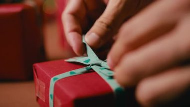 Kırmızı bir Noel hediyesi için yeşil bir kurdele bağlayan ellerinizi kapayın, bayram kutlaması için hazırlanın..