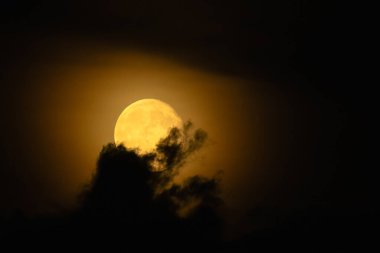 Gece gökyüzünde parlayan bir dolunay kısmen bulutlarla kaplı..