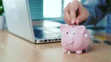 İş kadını eli, ofis masasındaki domuz kumbarasına para ya da para koyuyor. Para biriktirme kavramı.
