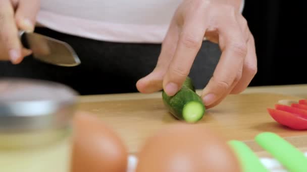 Női kéz segítségével konyhakés vágás friss uborka, hogy az egészséges szendvics receptek fa vágódeszka, Közelkép.