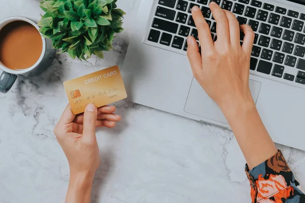 Top view, Woman customer hands holding credit card and using laptop computer for online shopping on desk, online payment concept.