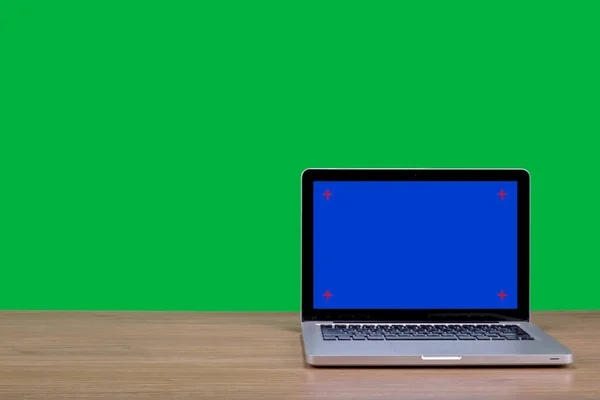 Blue screen laptop computer sitting on wooden desk with chroma key green screen background. Work from home concept.