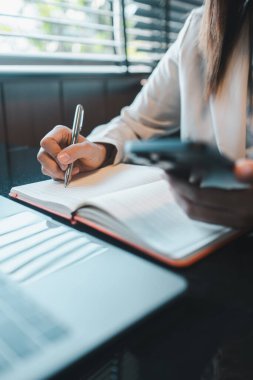 İş kadını, modern ofis ortamındaki bir masada defter ve akıllı telefonla birden fazla iş yapıyor..