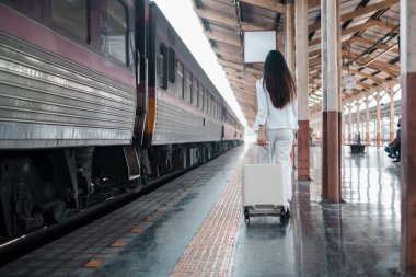 Tren peronunda bagajı olan bir kadın, seyahat macerasına atılmaya hazır..