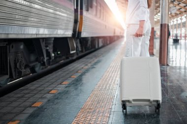 Gün doğumunda tren peronunda bekleyen bavullu kişi yolculuk macerasına hazır..