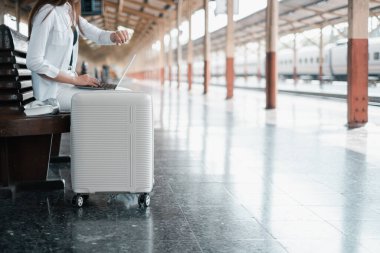 Tren istasyonunda bir bavulun üzerinde oturan kişi, seyahat ve teknolojiyi sembolize ediyor..